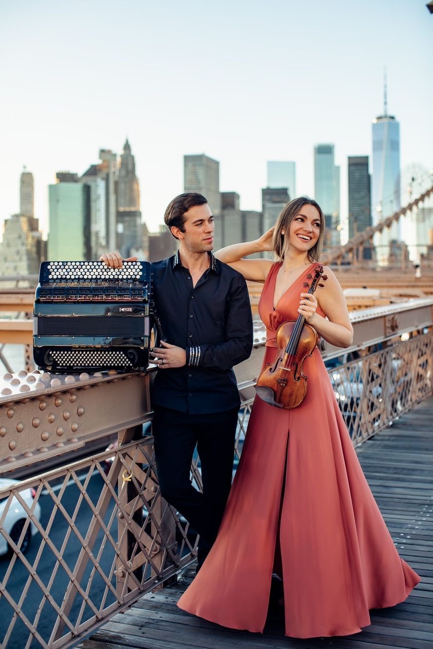 mężczyzna trzymający akordeon i kobieta trzymająca skrzypce stoją przy balustradzie mostu
