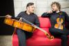 two men sitting on the couch holding a cello and violin